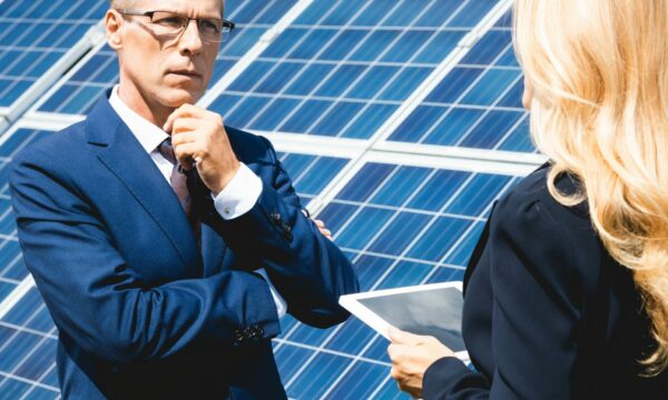 Handsome businessman and businesswoman talking and holding digital tablet with solar panels on the side