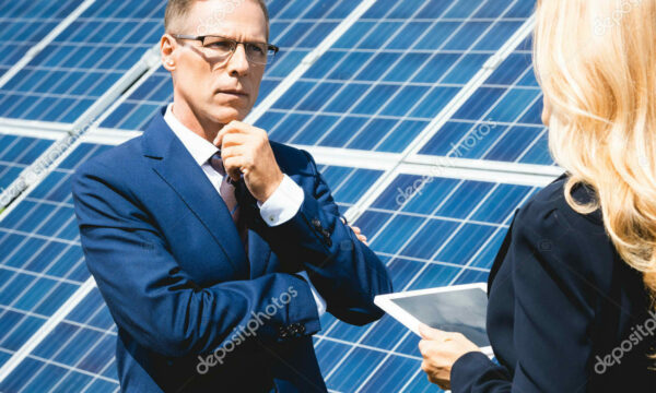 Handsome businessman and businesswoman talking and holding digital tablet with solar panels on the side