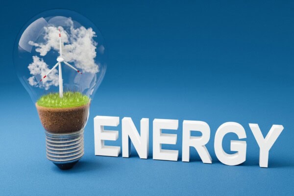 single lightbulb with minature wind turbine inside; green soil and clouds; renewable clean energy concept; 3d illustration